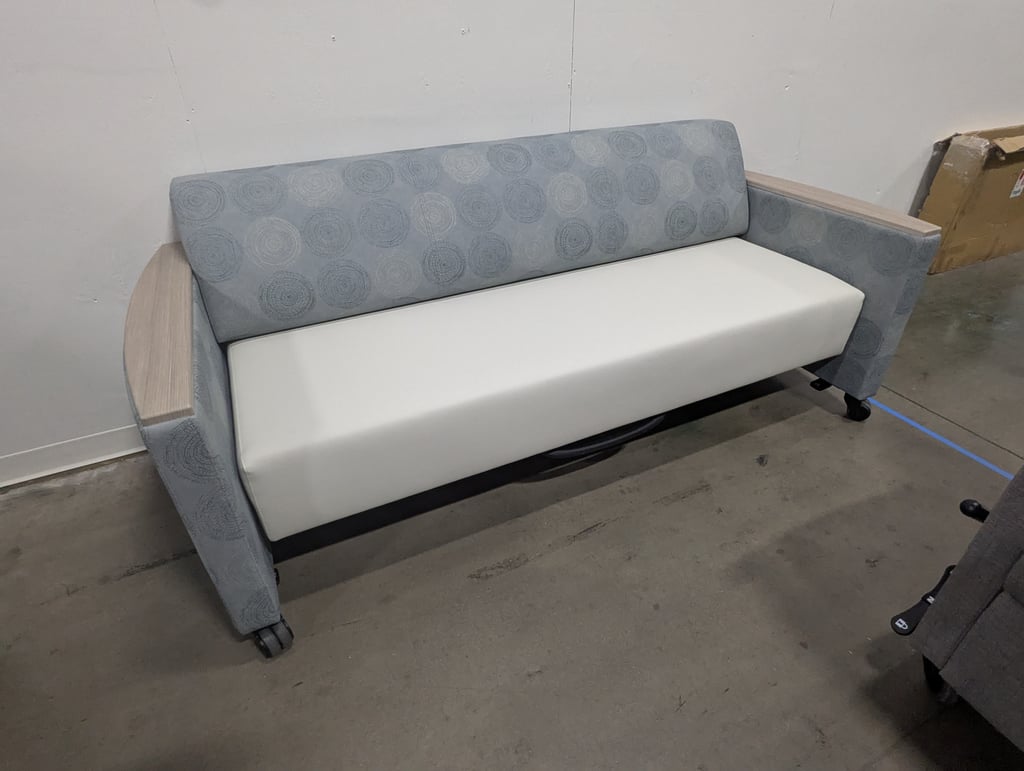 A two-seat bench in circle-patterned grey upholstery with wooden arm caps, on casters