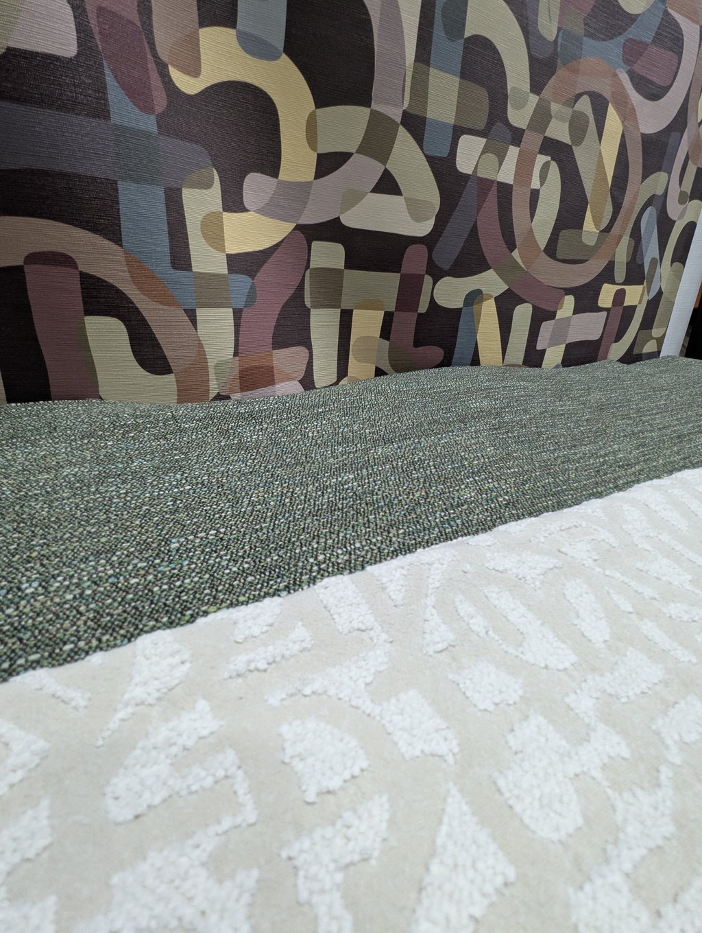 A close view of abstract patterned wallcovering in muted earth tones above a cream textile with raised leaf motifs