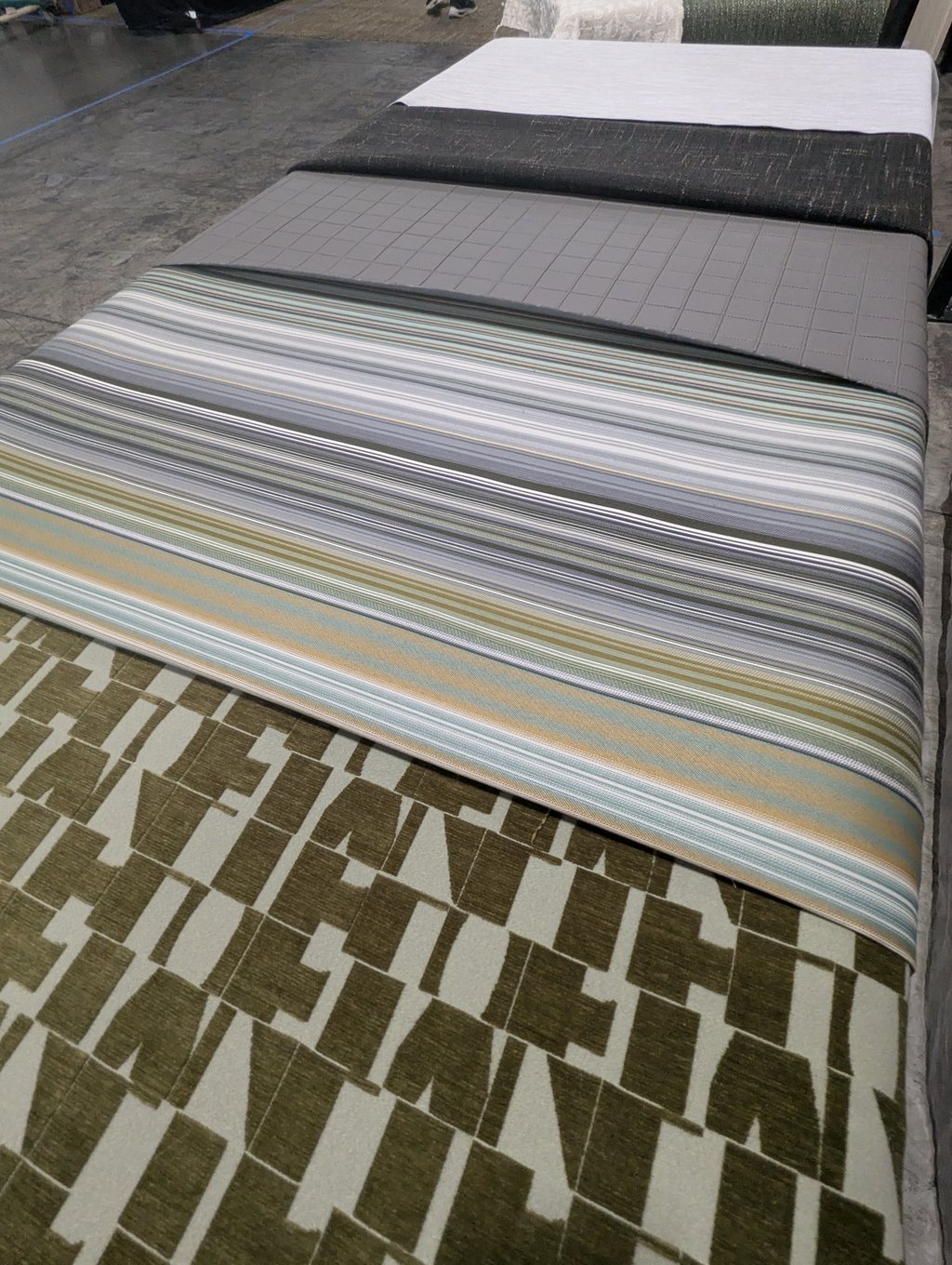 Striped, quilted and textured upholstery samples layered on a green and cream geometric carpet