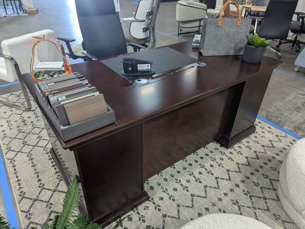 A dark wood executive desk holding wood sample cards, a card holder and a potted succulent