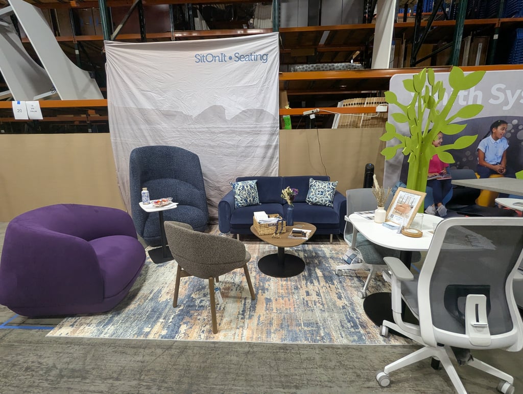 A purple pouf, blue armchairs and a small sofa around a coffee table at the SitOnIt Seating booth