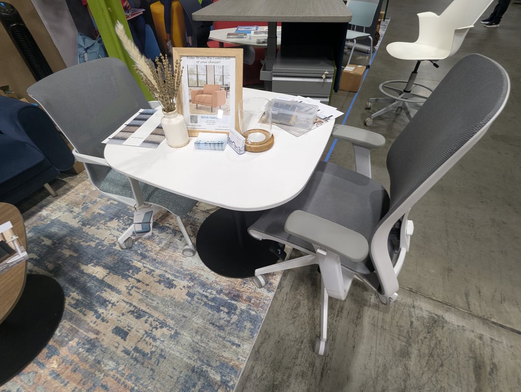 Two grey mesh office chairs at a white table with dried flowers and a SitOnIt Seating prize draw sign