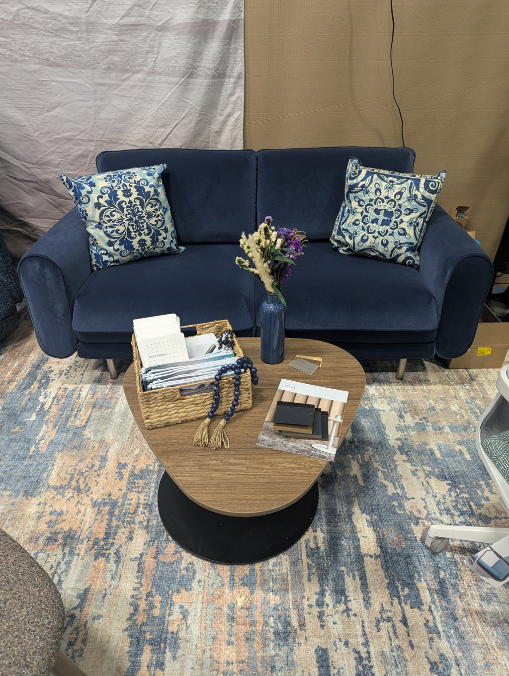 A deep blue velvet loveseat with patterned cushions and a coffee table holding a basket of fabric samples