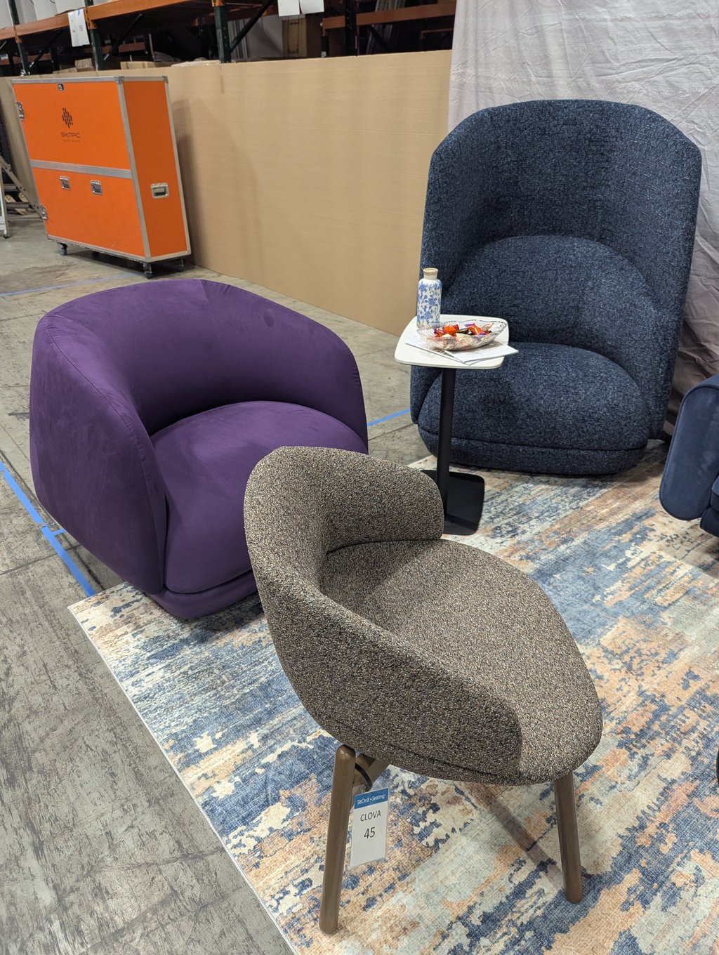 A purple lounge chair, a tall blue high-back chair and a grey seat around a side table with a bowl of sweets