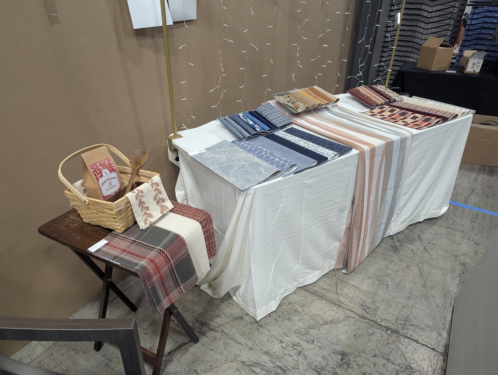 Folded patterned swatches on a display table with a wicker basket of treats and string lights behind
