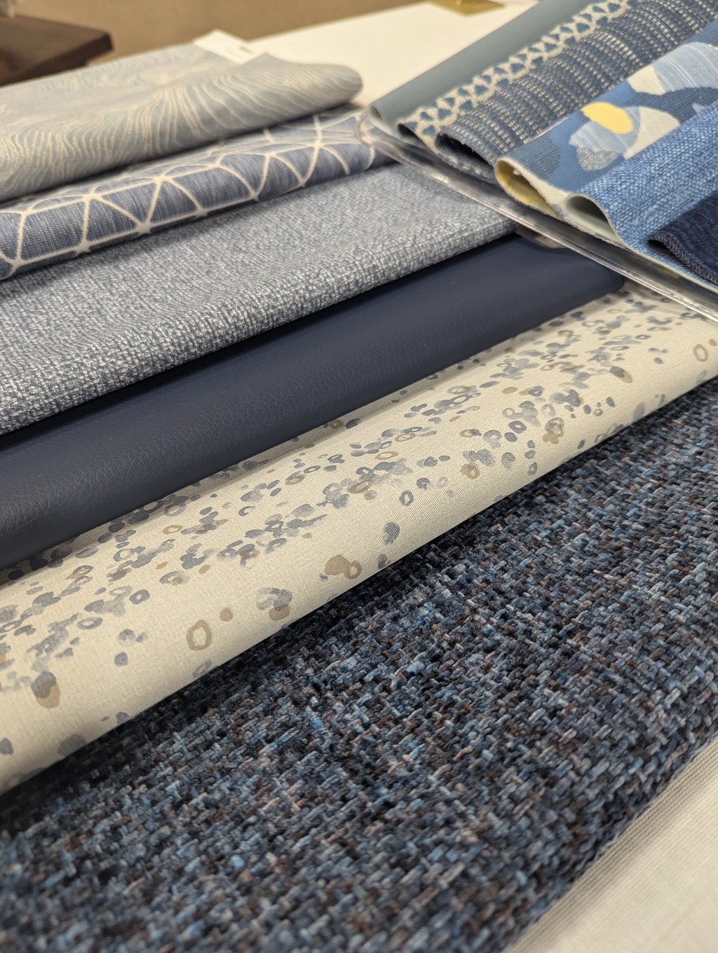 Stacked upholstery swatches in blues and neutrals, from geometric lattice to navy leather and woven textures