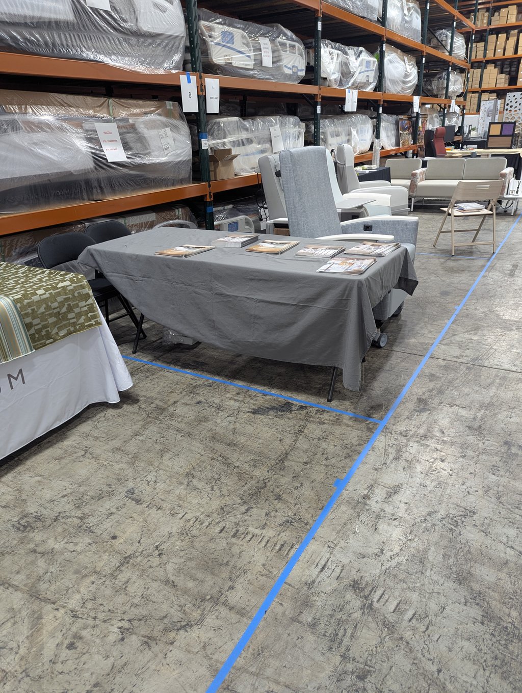 Chairs and a cloth-covered brochure table at booth 8, with wrapped furniture on the racking behind