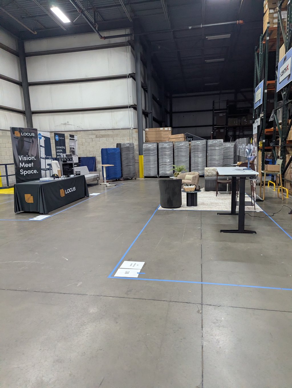 The Locus table and Vision. Meet Space. banner with stacked chairs and racking filling the warehouse behind
