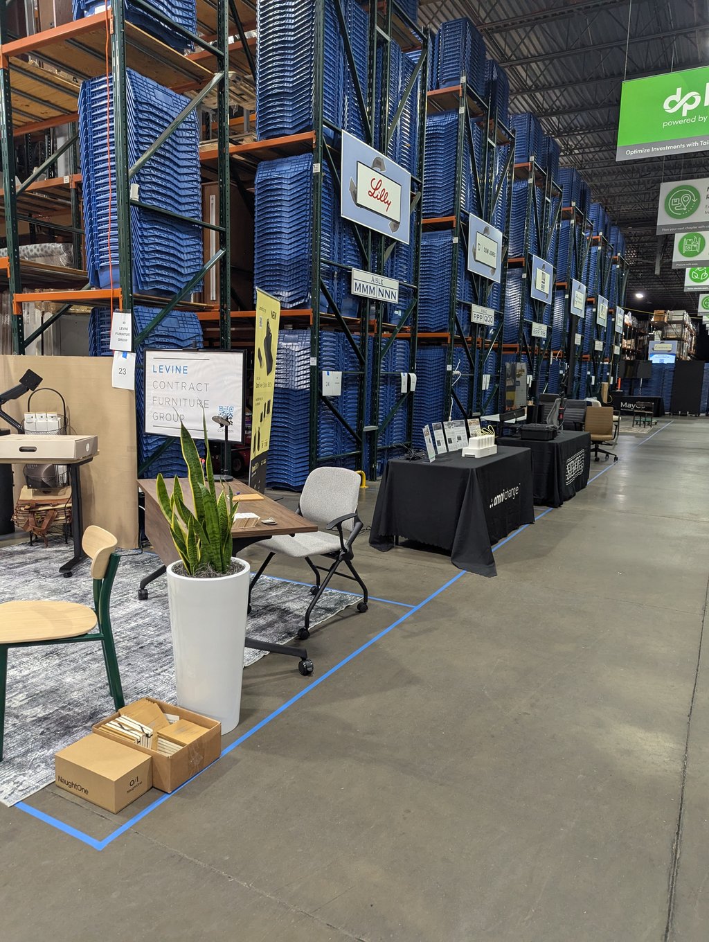 A booth of chairs, tables and a potted plant beneath the Lilly aisle sign and the Levine Contract Furniture Group display