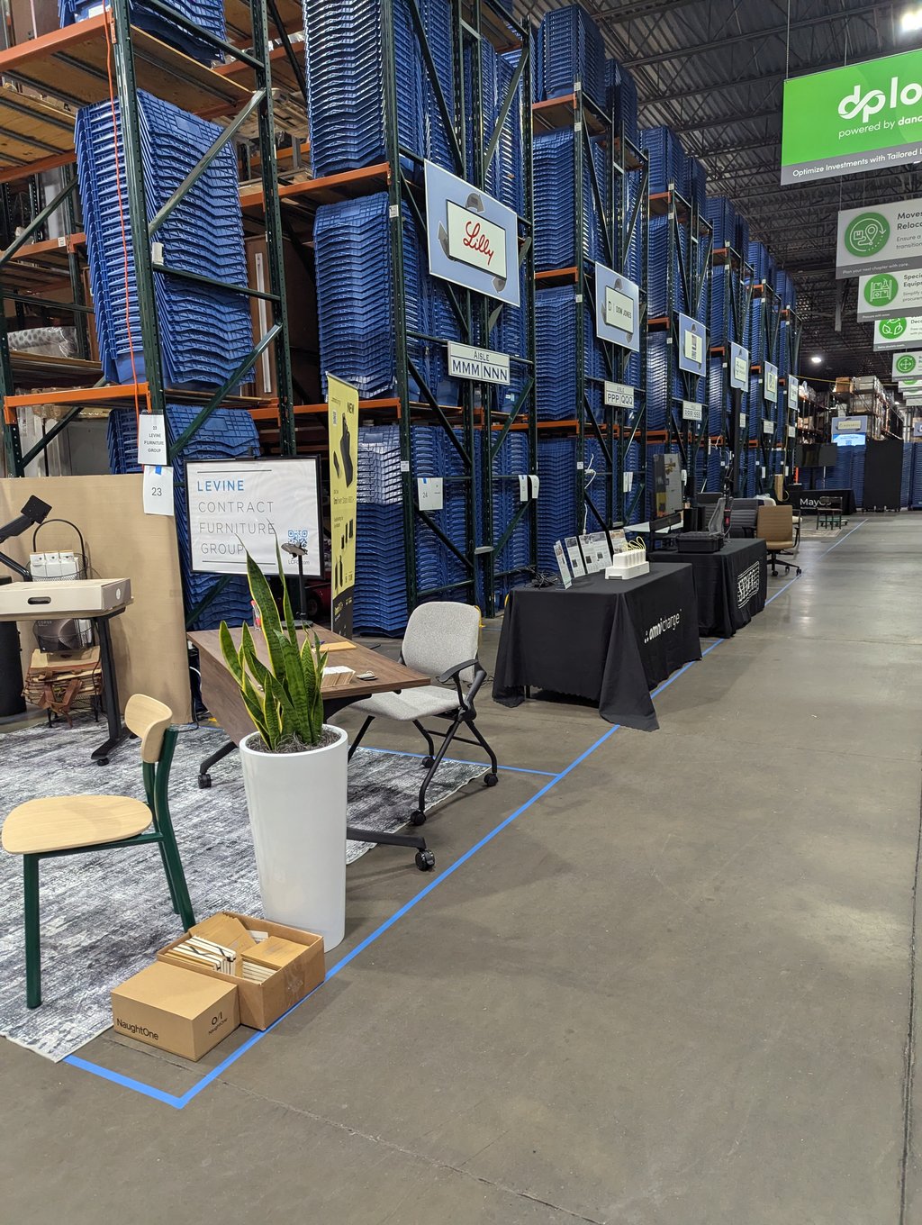 Rows of blue bins on tall racking above the Levine Contract Furniture Group stand under the Lilly sign