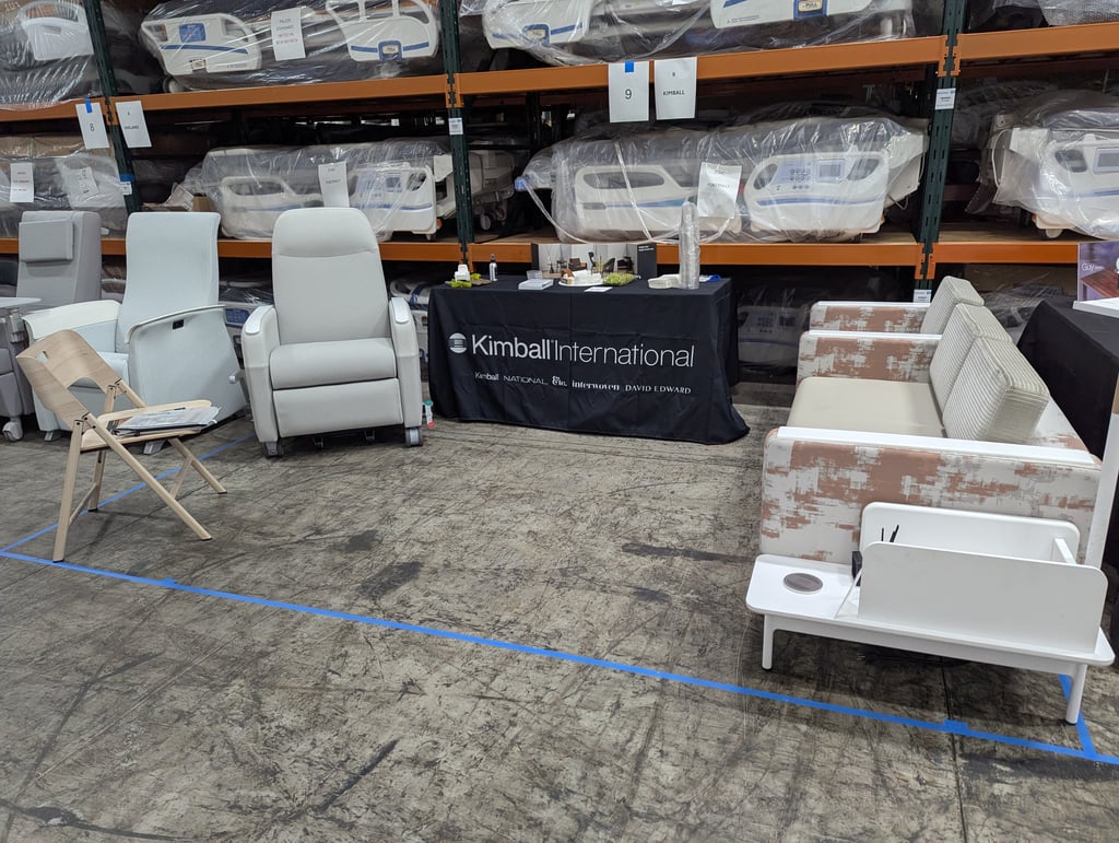 Upholstered chairs at the Kimball International booth, number 9, with wrapped hospital beds on the racking behind