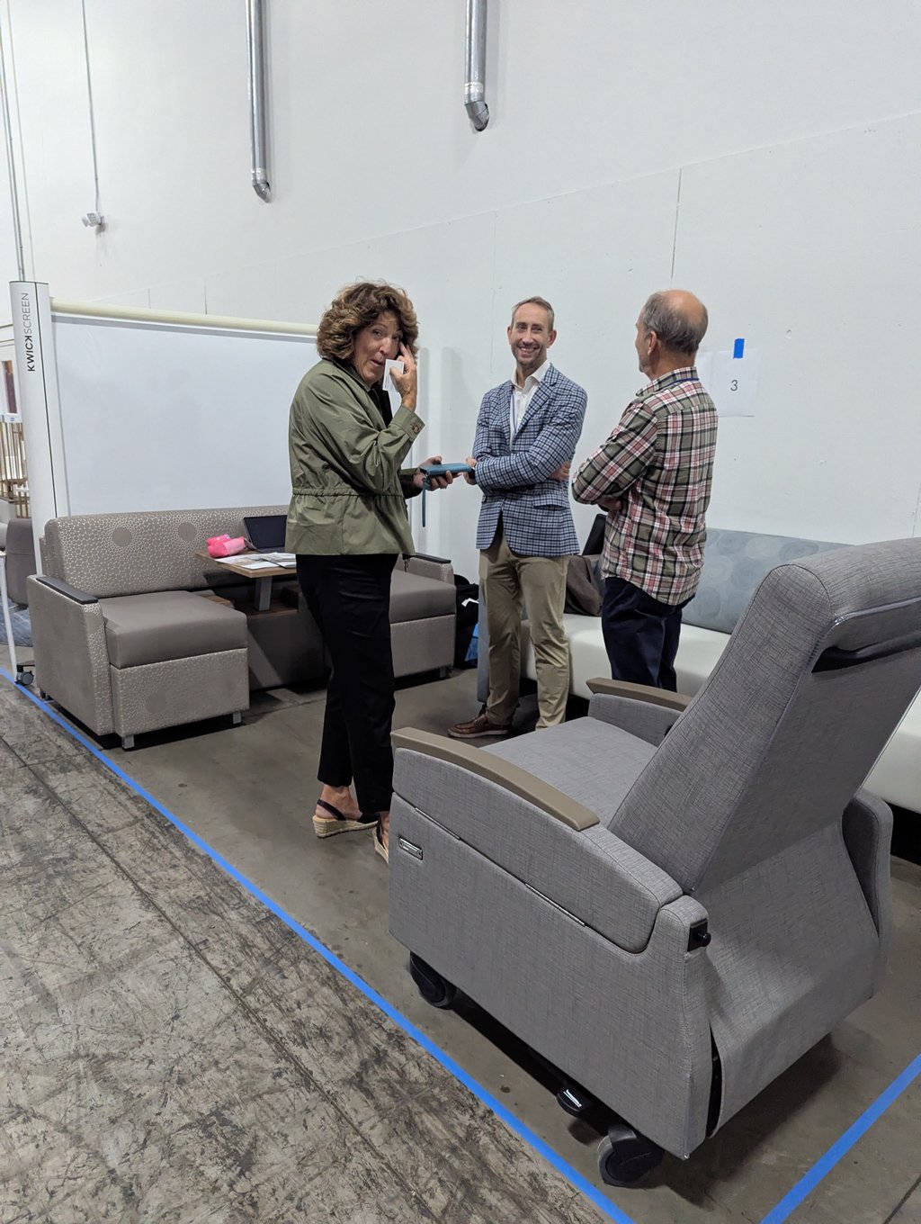 Three attendees in conversation among sofas and a grey recliner beside the KwickScreen display at booth 3