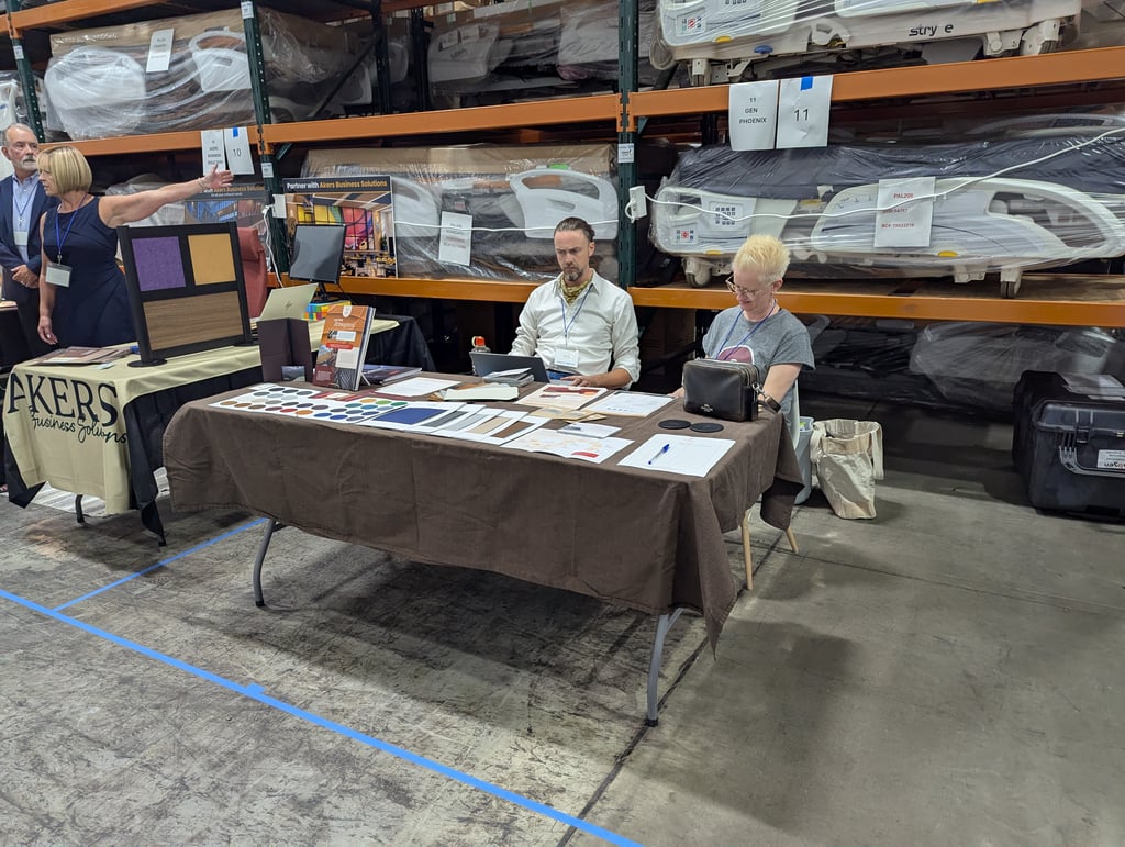 Two exhibitors seated behind brochures, colour swatches and a laptop at the Akers Business Solutions table