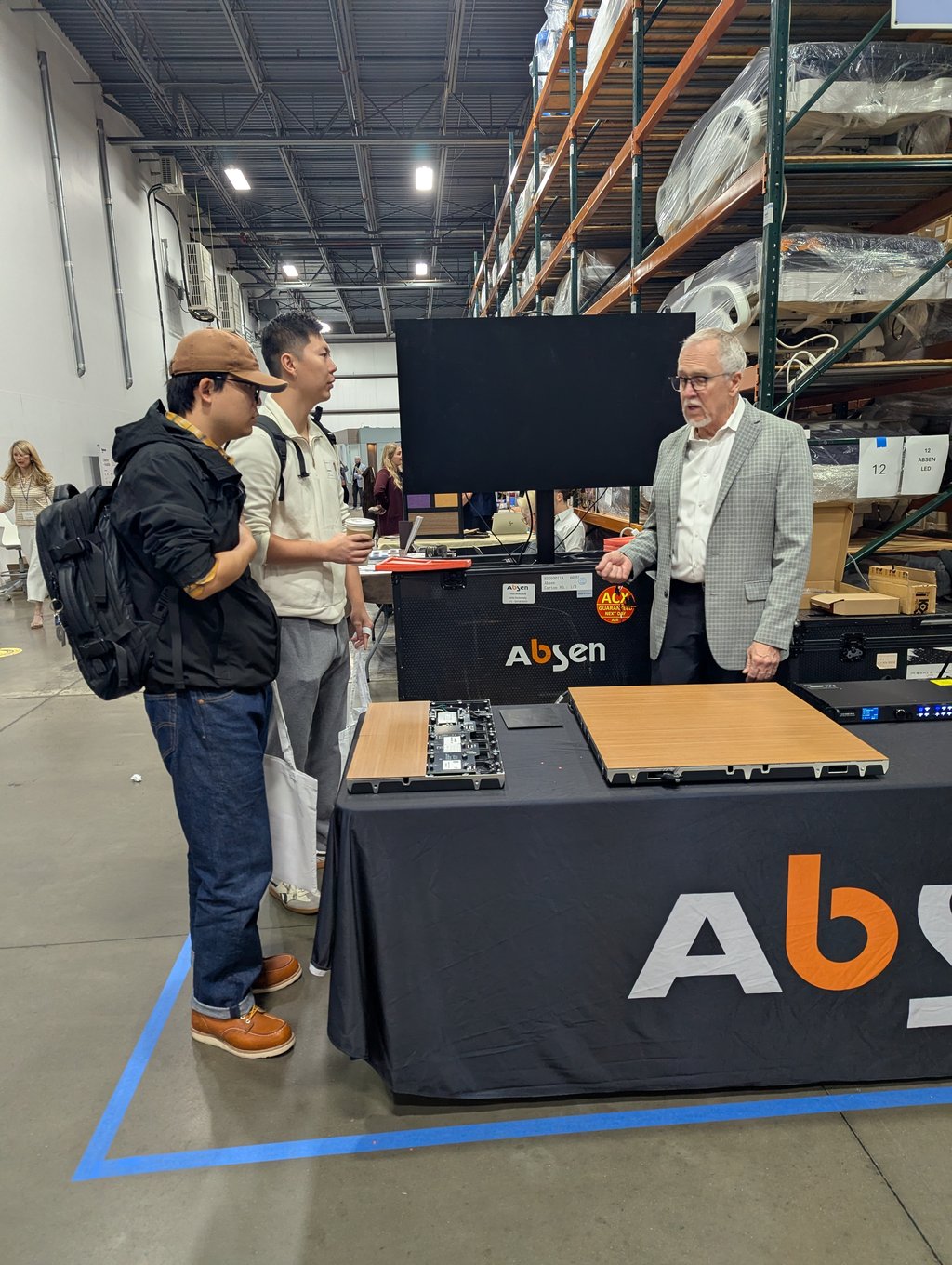 An exhibitor explaining display panel components to two attendees at the Absen booth