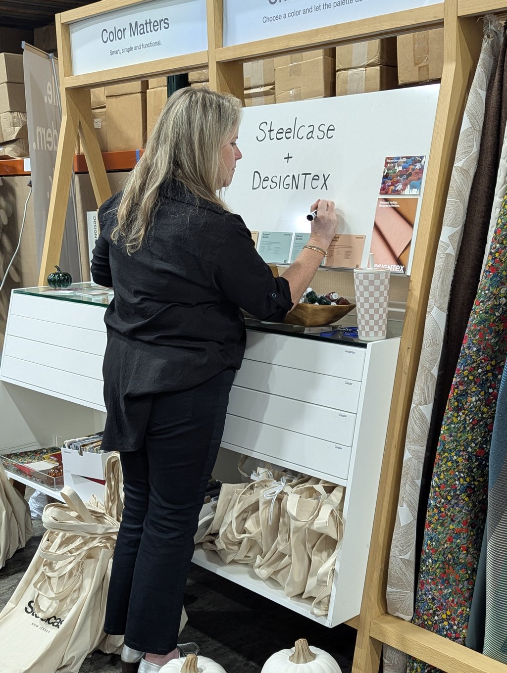 An attendee writing on the Steelcase and Designtex Color Matters board among fabric samples and tote bags
