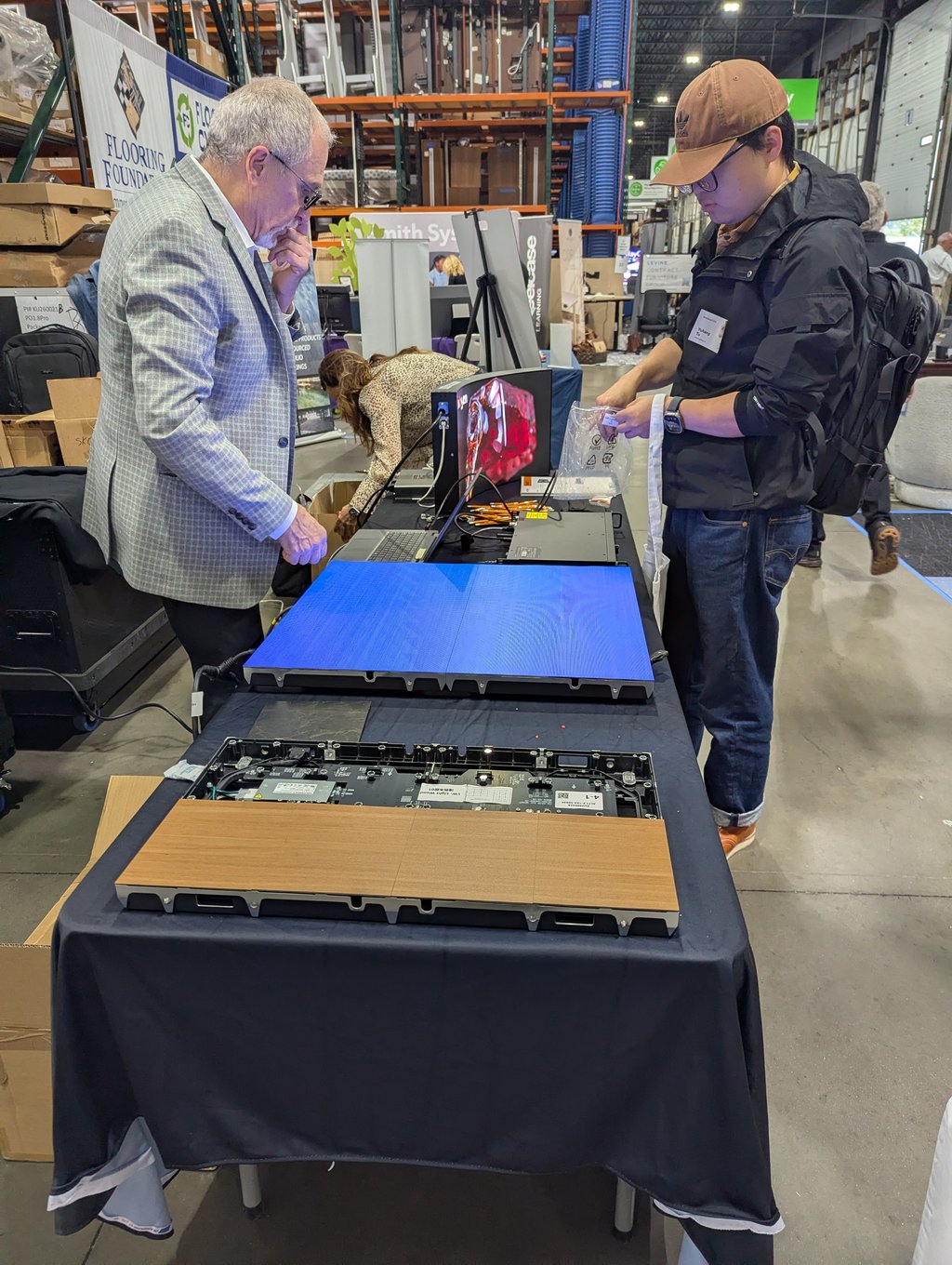 Two attendees examining electronic display panels and components in front of the Flooring Foundation banner