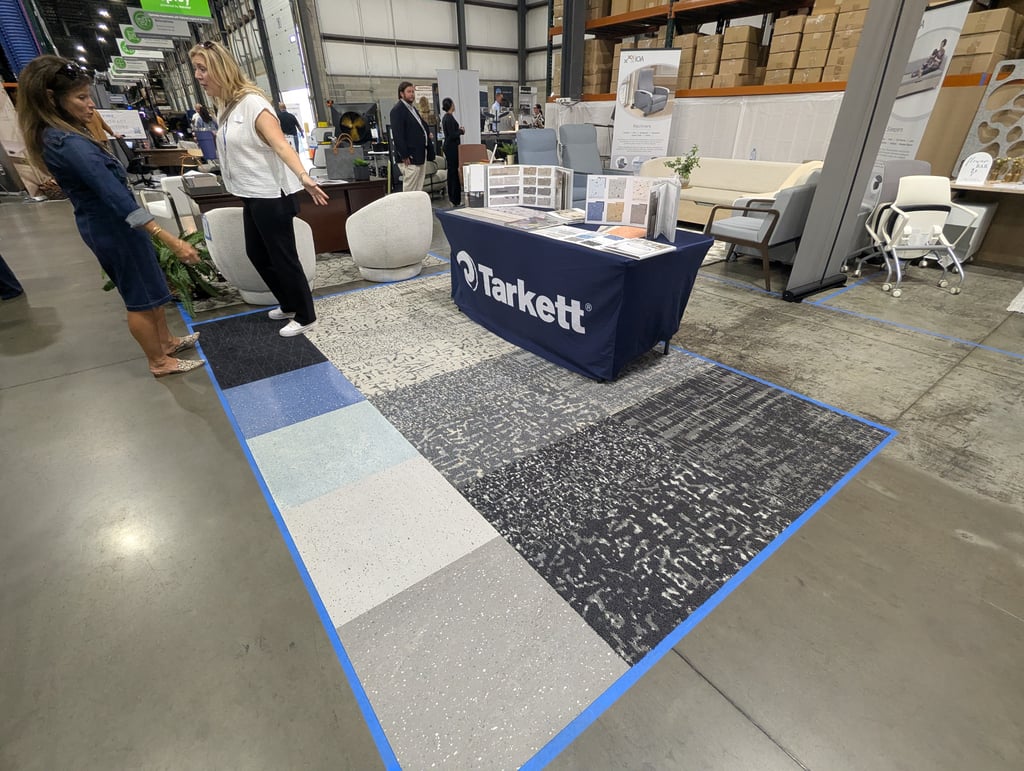 Large carpet and tile samples laid out on the floor at the Tarkett stand with attendees talking nearby