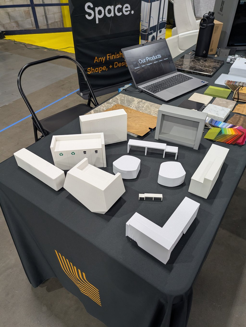 White architectural models, material samples and swatches on a table beside a laptop showing a product page
