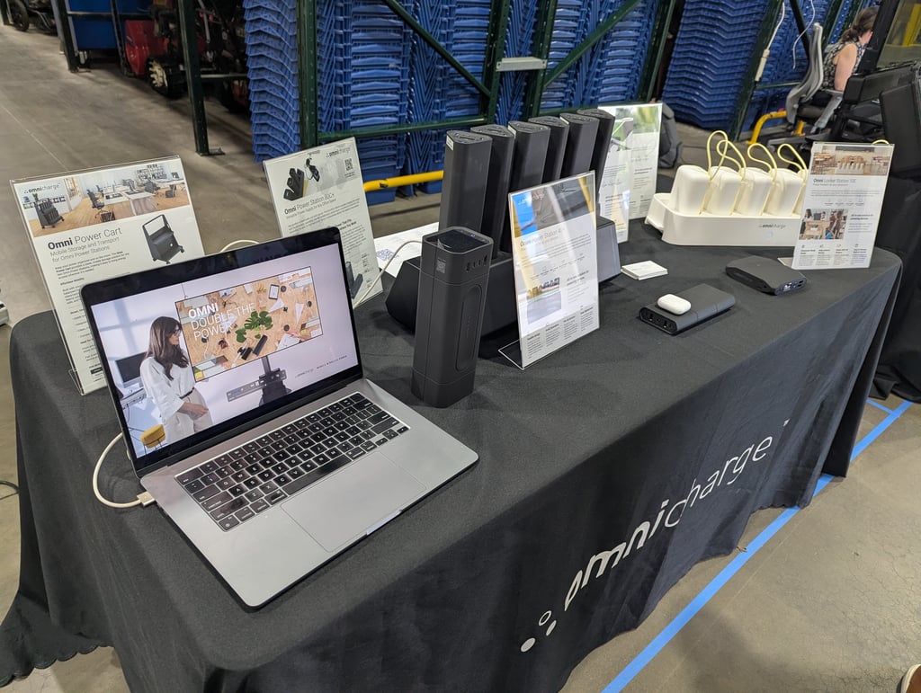 Rows of power banks and charging pods on the Omnicharge display table beside a laptop and signage