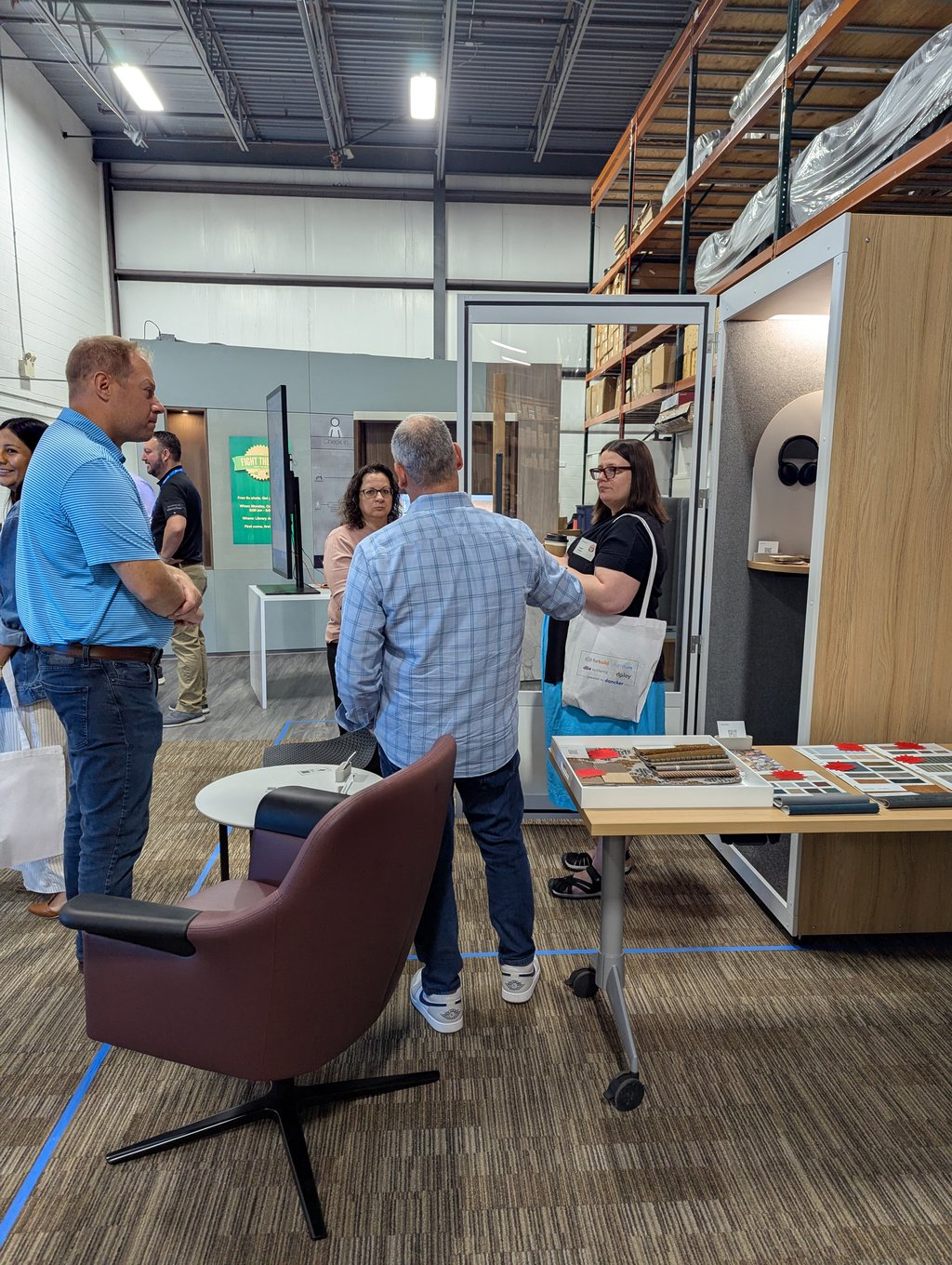 Attendees talking around a small glass meeting booth and sample table below the check in sign