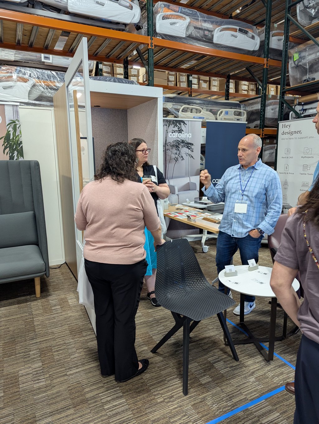 Attendees talking at the Carolina stand among fabric and material samples, with a designer support poster behind
