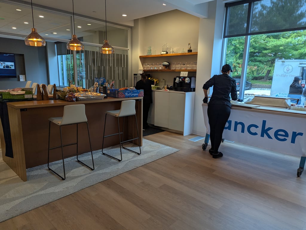 A wooden catering counter piled with snacks and coffee machines under pendant lights, with the coffee truck outside the window
