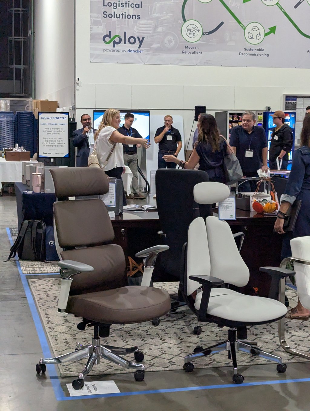 Office chairs on display with attendees talking beneath the dploy Logistical Solutions banner