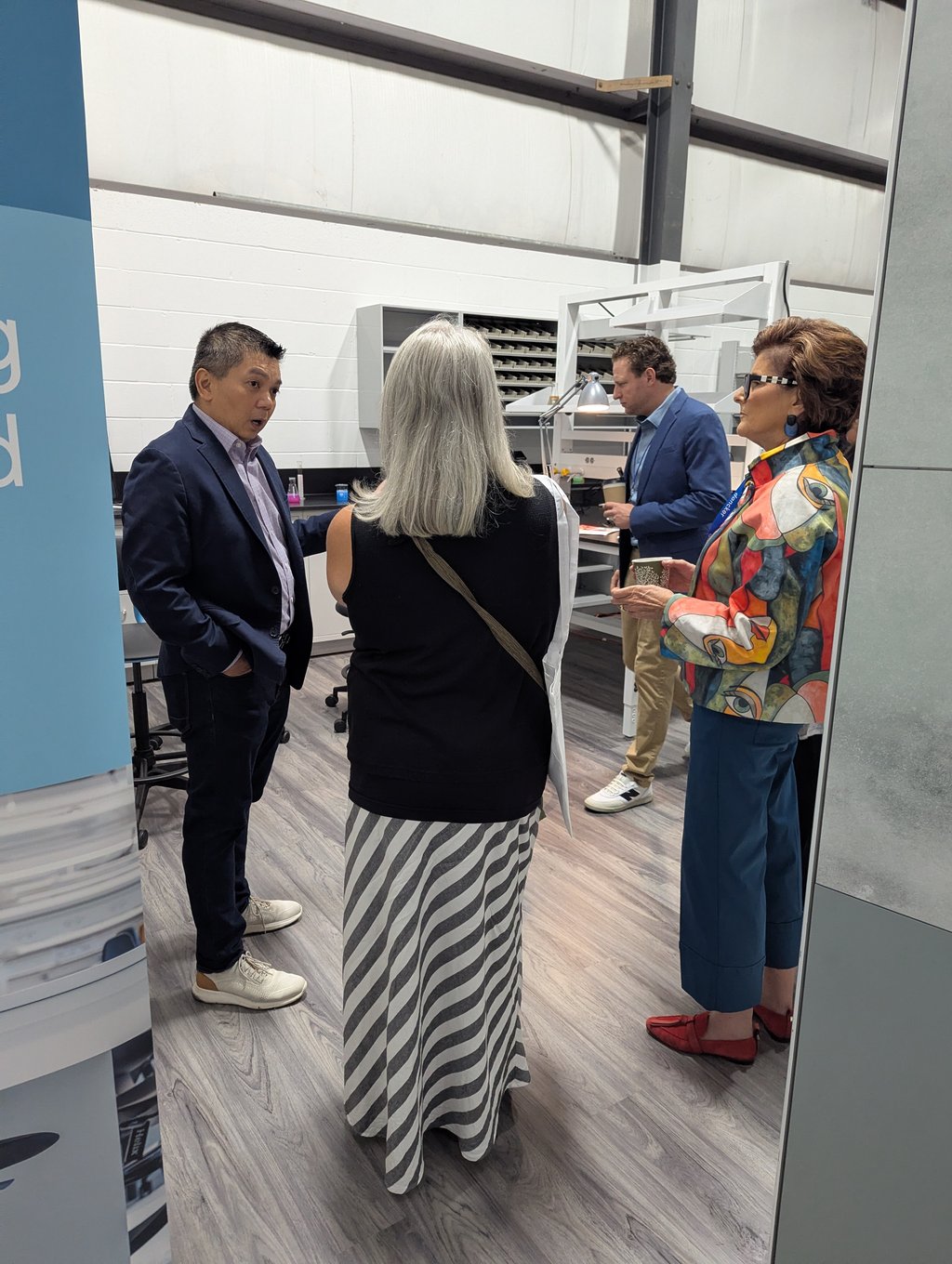 Four attendees talking with drinks in a workshop space with shelving and task lamps