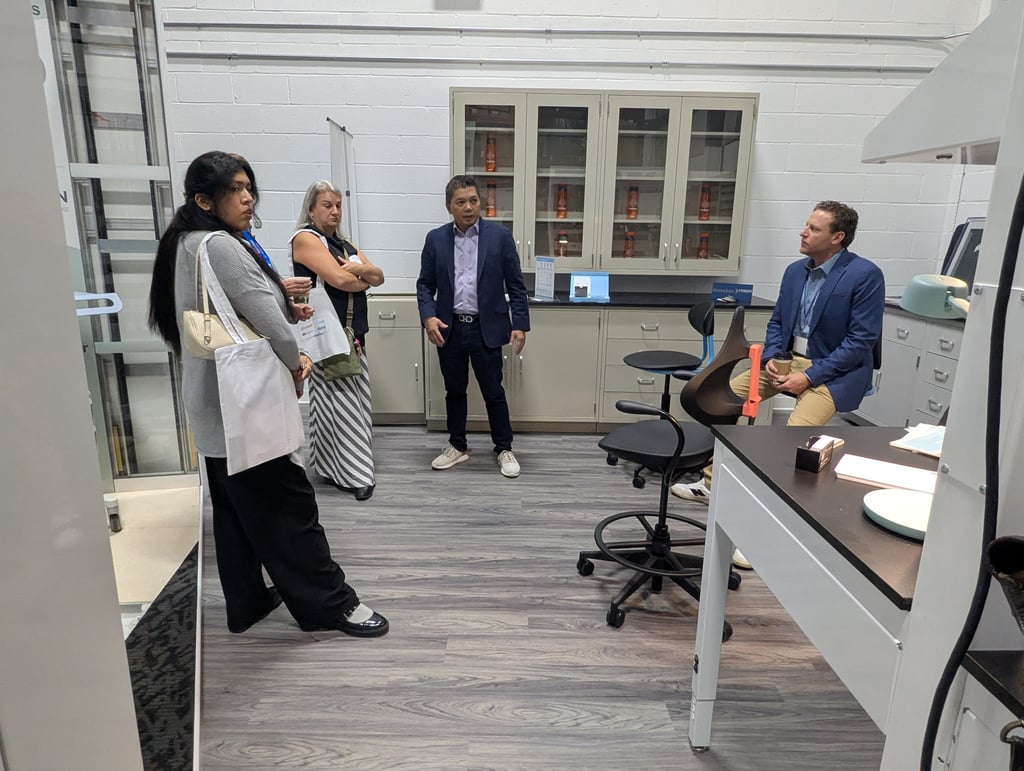 Five attendees gathered in a lab room with grey cabinets, glass cupboards and a workbench with stools