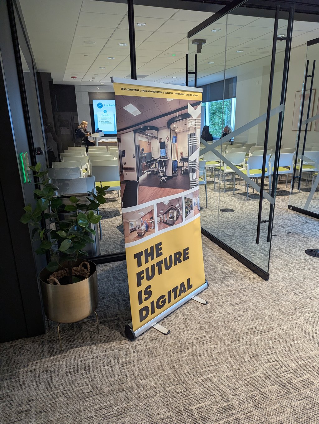 A tall yellow banner reading The Future Is Digital outside a glass meeting room set with rows of chairs