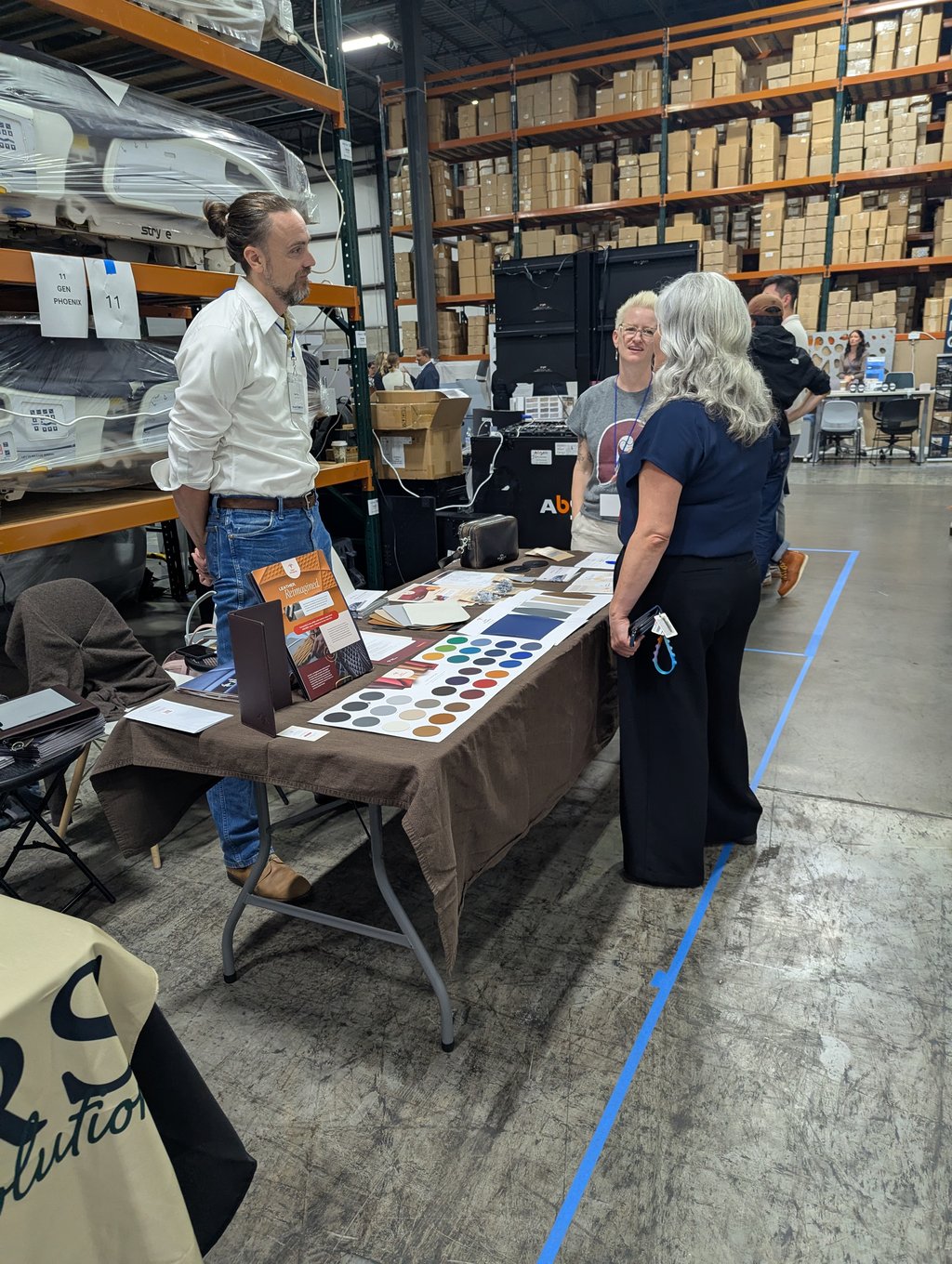 Three attendees in conversation over colour swatches at the Gen Phoenix table, booth 11