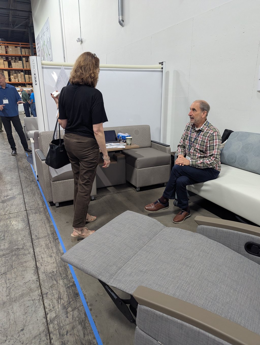 An attendee seated on modular seating talking with a visitor beside the KwickScreen panel