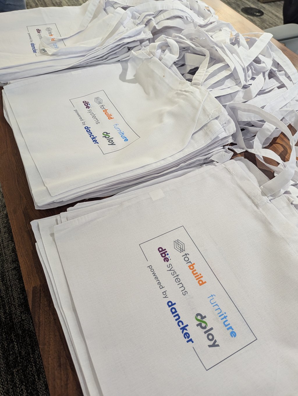 Stacks of white cloth tote bags printed with the dploy powered by dancker logo