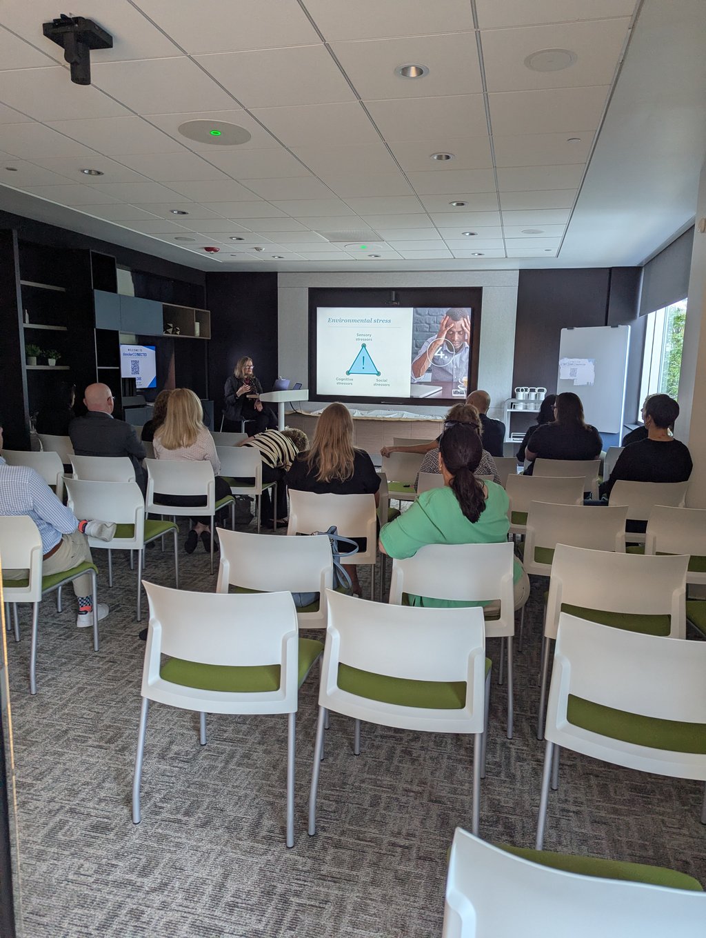 Attendees seated in rows facing a presenter and a screen showing an Environmental stress slide