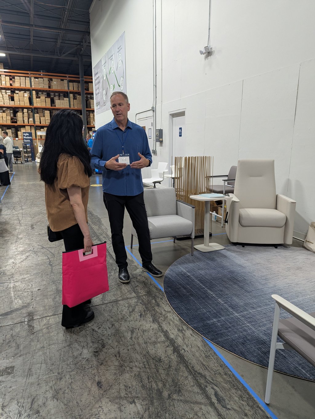 Two attendees in conversation beside a seating display, one holding a pink tote, under the Agile Modern Quick sign