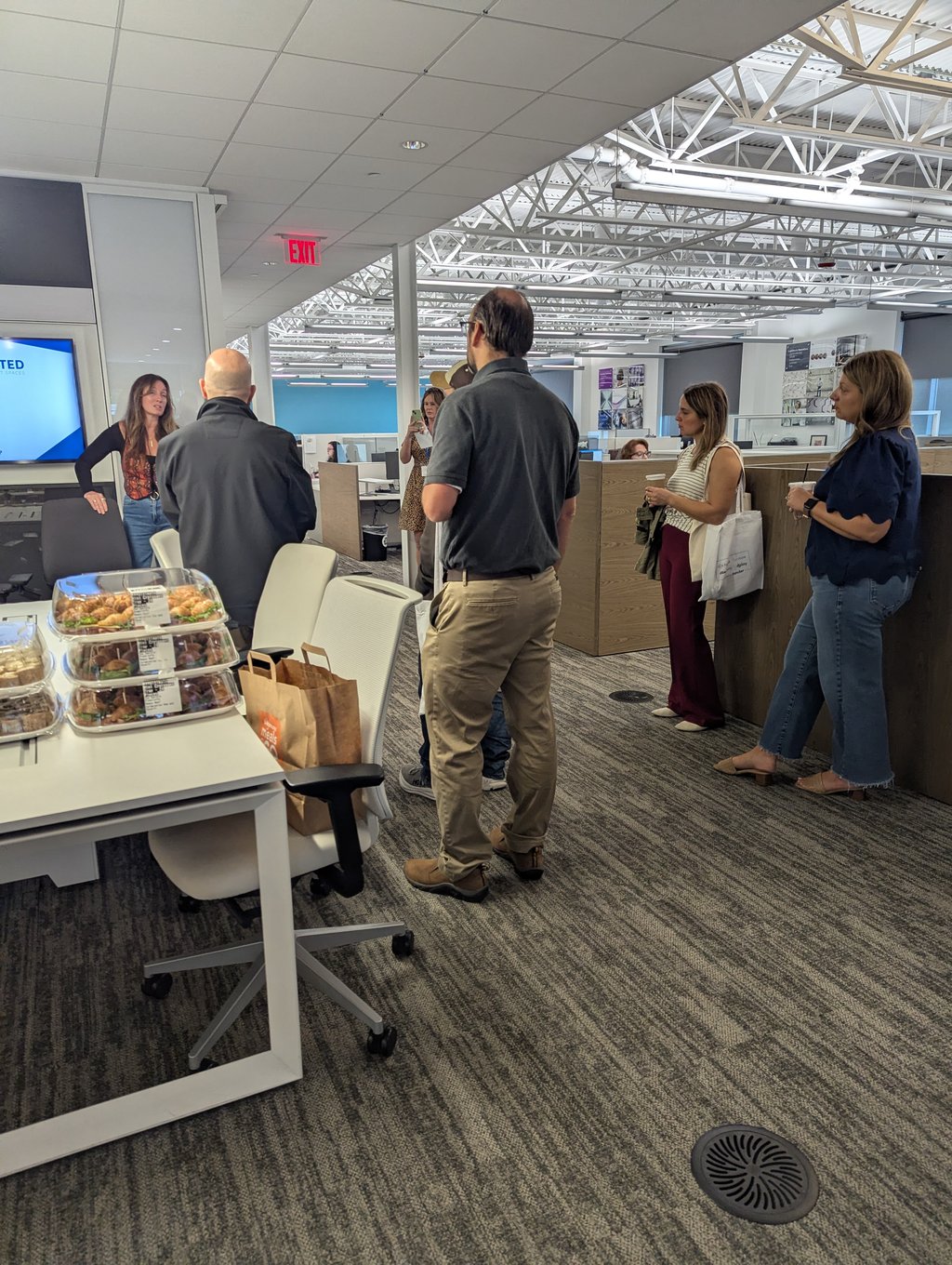 Attendees gathered near a table of sandwich trays and paper bags in the open plan office