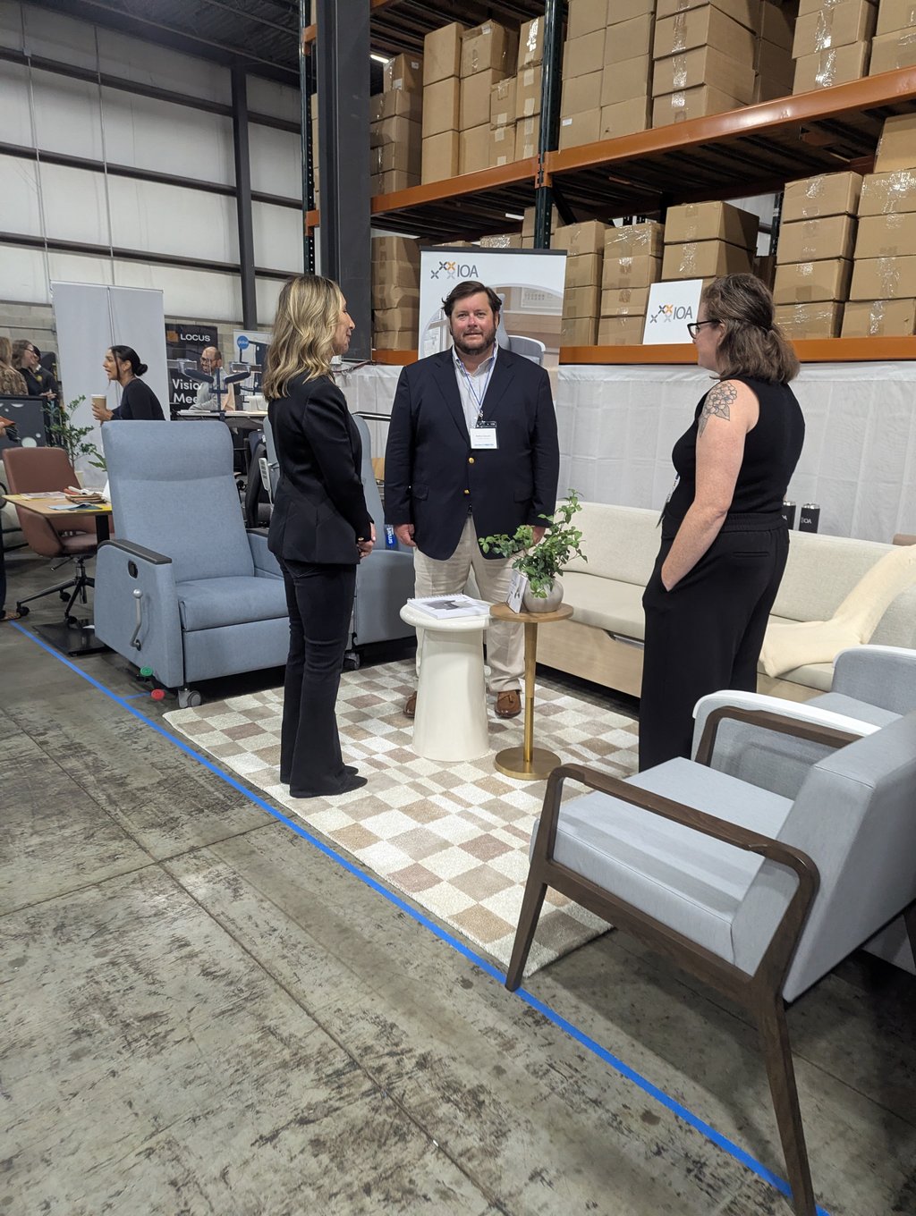 Three attendees talking among chairs and a planted side table in front of the IOA banner