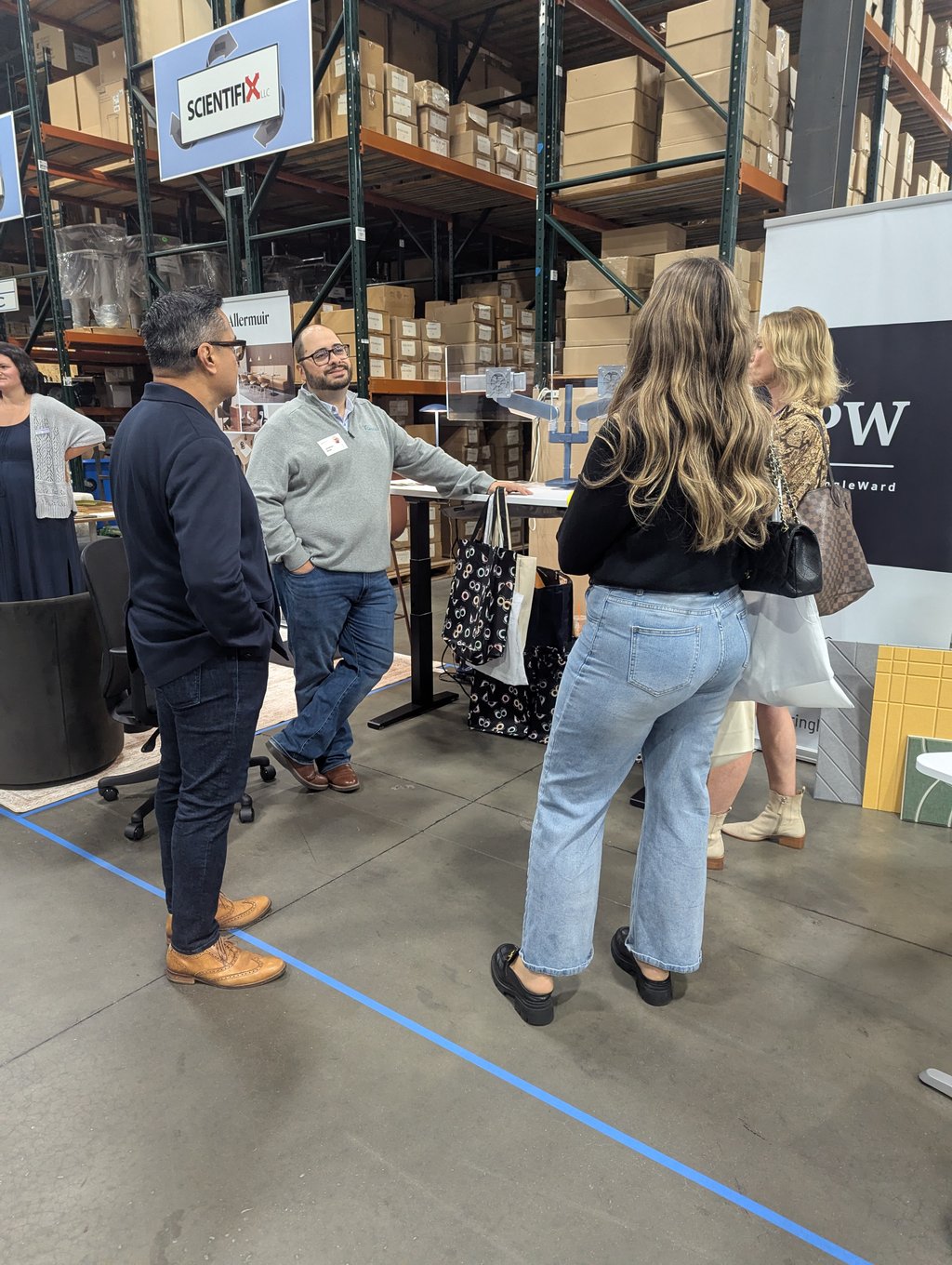 A group of attendees talking at the Scientifix booth in front of tall shelving and stacked boxes