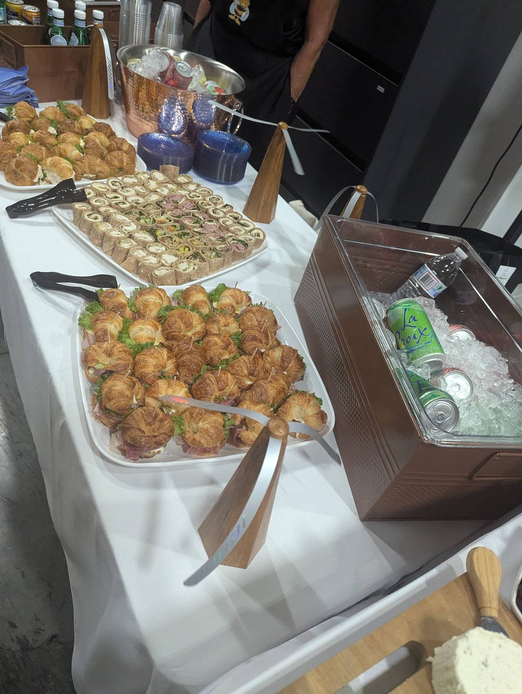Trays of croissant sandwiches and pinwheel wraps beside a copper bucket of iced drinks