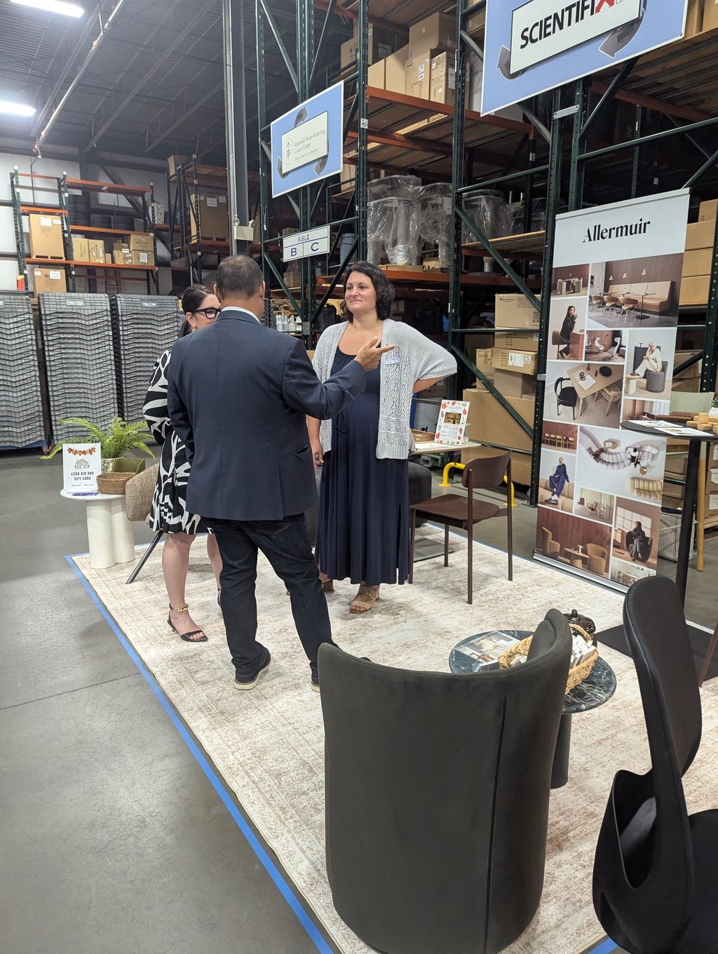 Three attendees talking beside chairs and a small table at the Allermuir stand