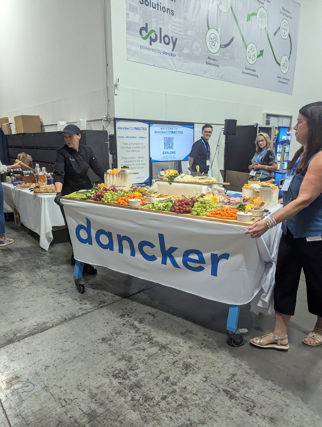 A catered display of fruit, vegetables and cheeses on the dancker table with staff and attendees behind