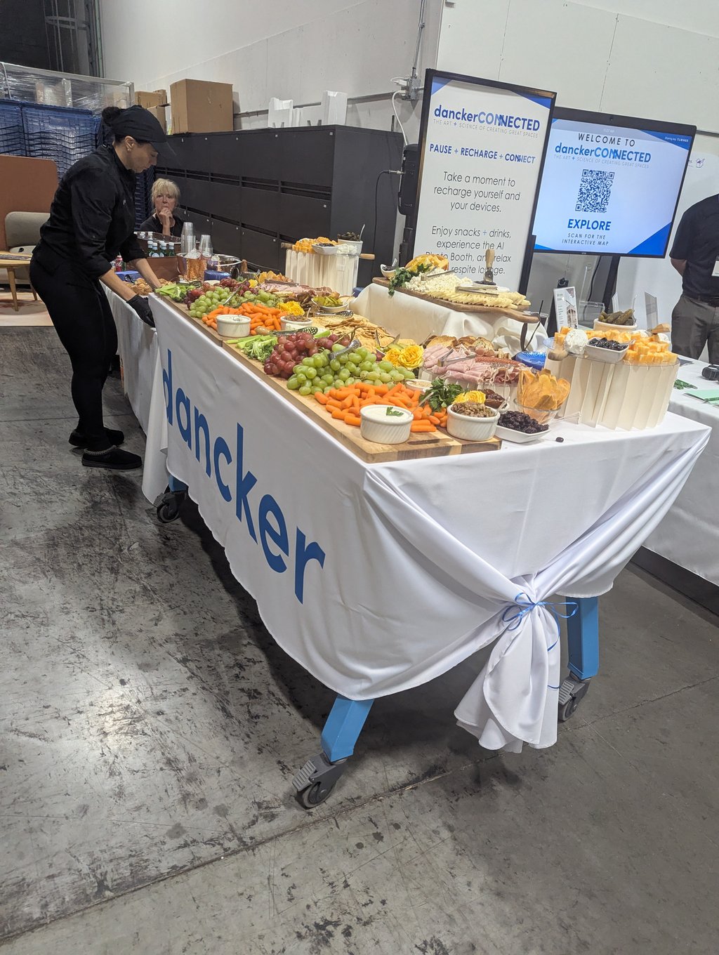A server arranging the grazing table of grapes, carrots, cheeses and meats below the Pause Recharge Connect screen