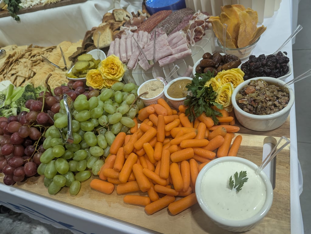 A close view of the grazing board with baby carrots, grapes, dips, deli meats and crackers garnished with yellow roses