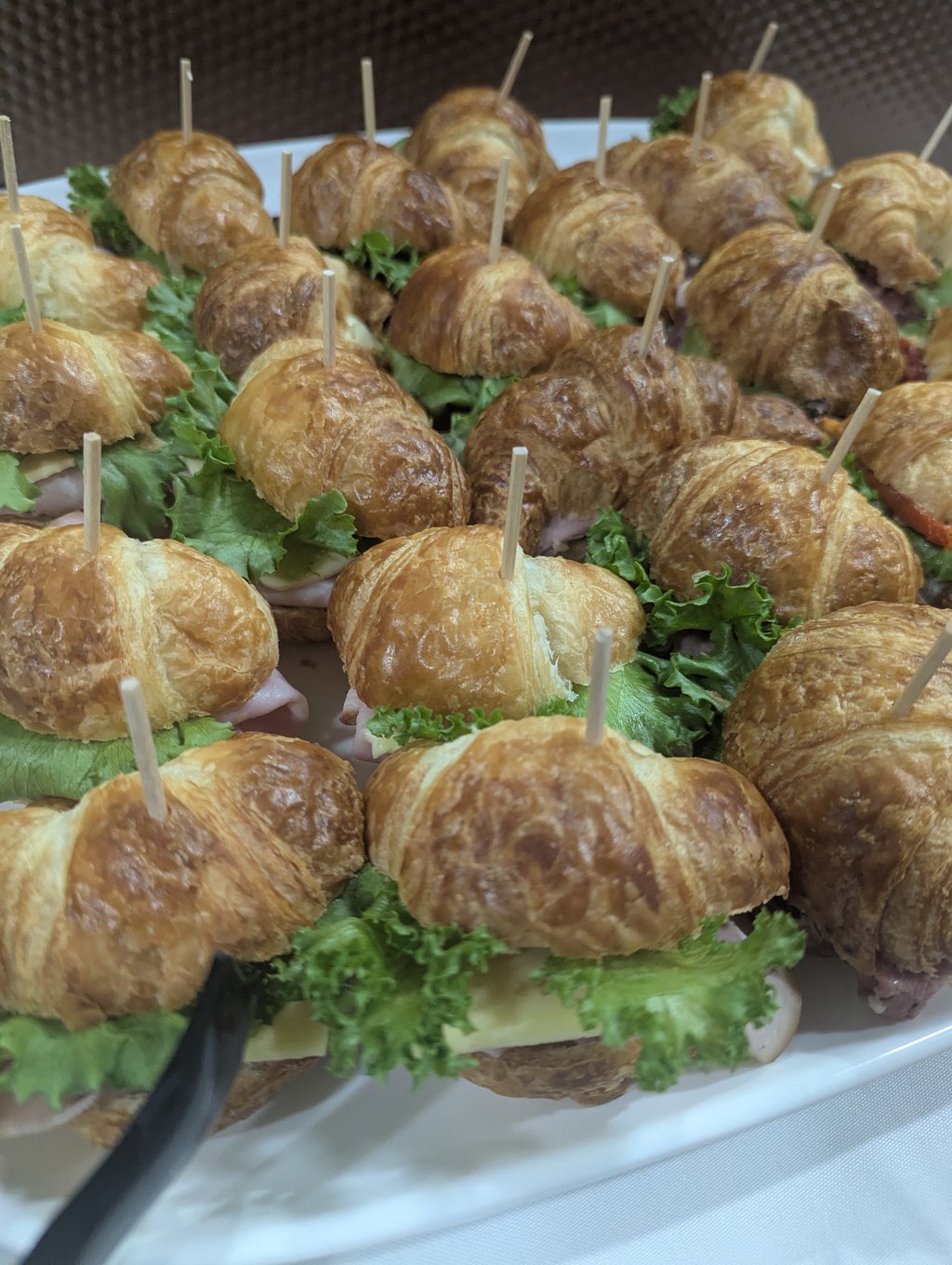 Rows of bite-size croissant sandwiches filled with lettuce, deli meat and cheese, each on a wooden pick
