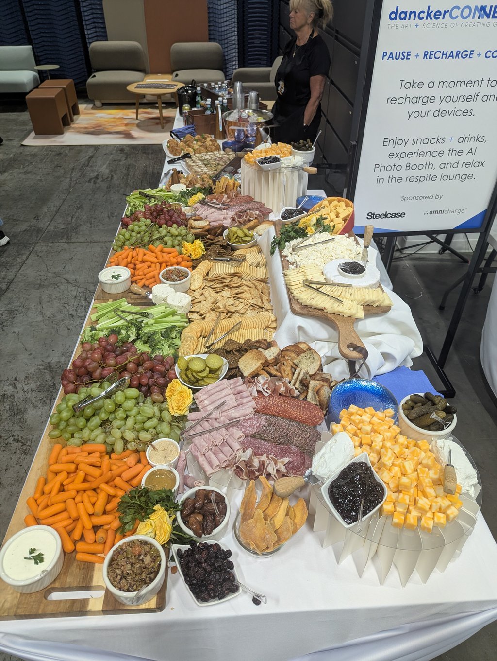 A server behind a long grazing table of cheeses, meats, crackers and fruit beside the Pause Recharge Connect sign