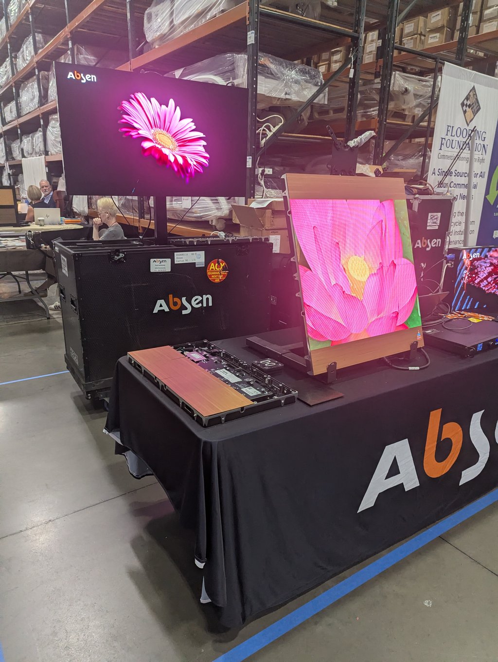 Large Absen LED screens showing bright pink flowers at the booth, with the Flooring Foundation banner behind