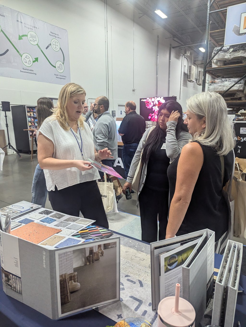 An exhibitor holding colour swatches at a sample table below the Sustainable Decommissioning and Asset Management banner