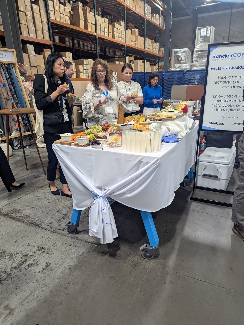 Attendees gathered around a buffet table of fruit and snacks beside the Pause and Recharge sign