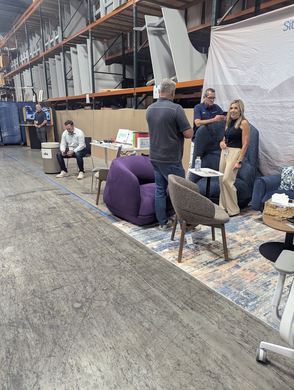 Attendees standing and seated around a furniture display of chairs and tables below tall industrial shelving
