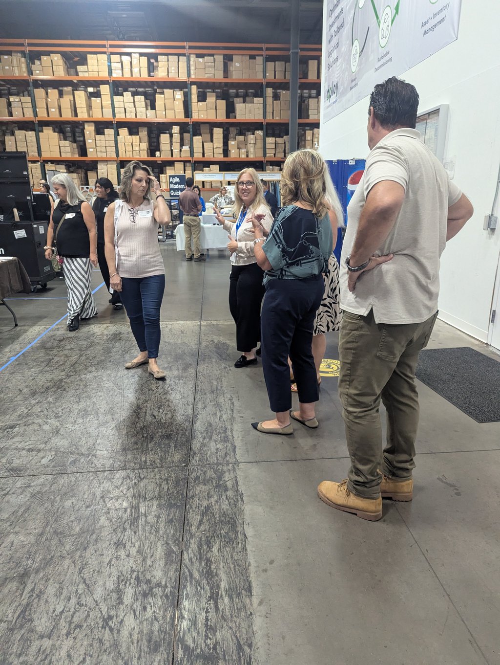 A group of attendees in conversation in a wide warehouse aisle below the Agile Modern Quick sign